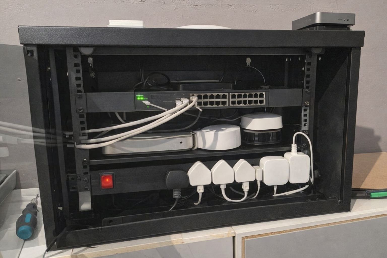 Ett svart nätverksskåp med switch, kablar och nätverksutrustning monterad i ett hem.